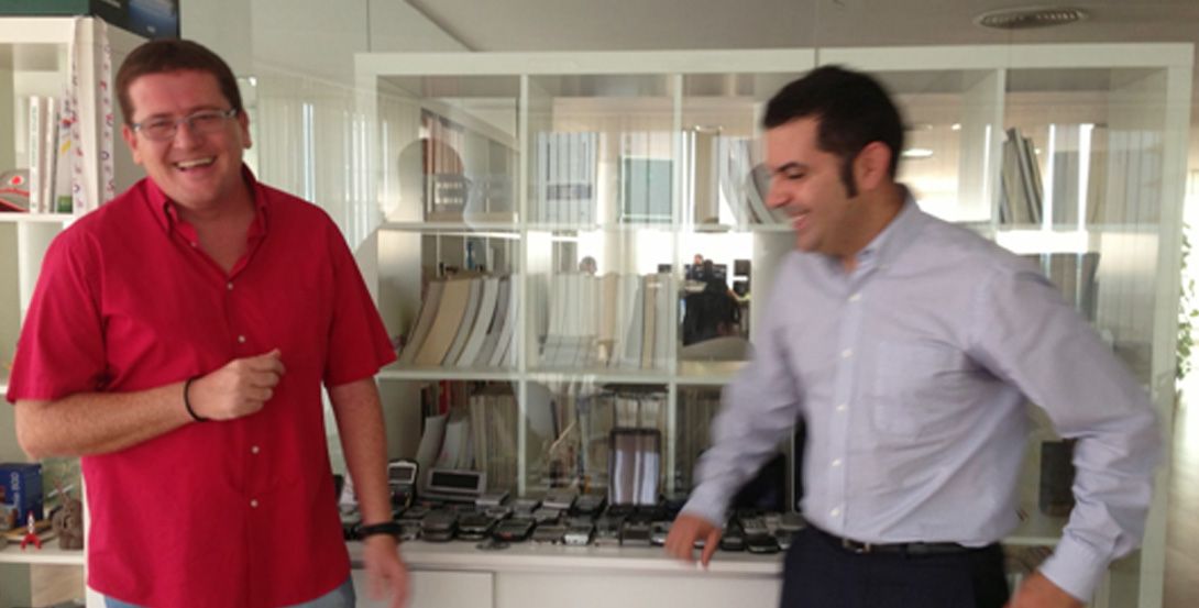 Juan Manuel Sáez de MVR Lab y Javier Pita de Neosistec, riendo distendidos en un despacho. hay decenas de móviles sobre un mueble y libros tras un cristal.